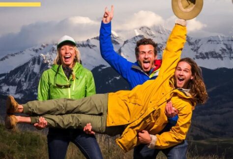 Three explorers waving from in front of a mountain