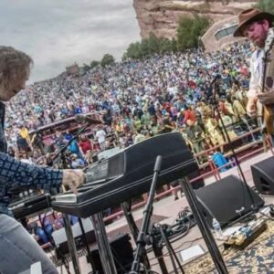 Two men on outside stage playing music and audience in background